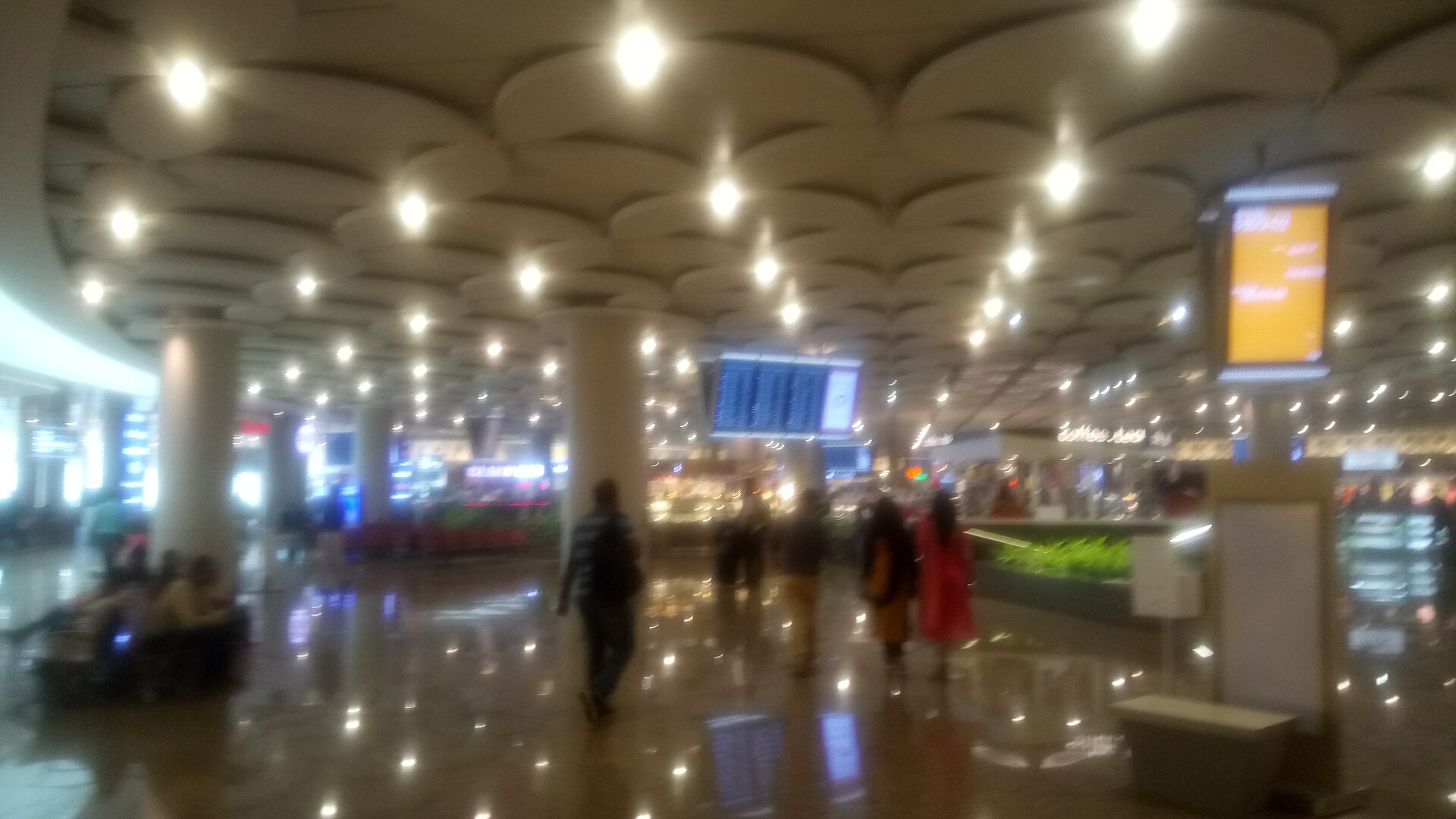 People walking through a busy airport departure lounge with international flight information boards in the background.