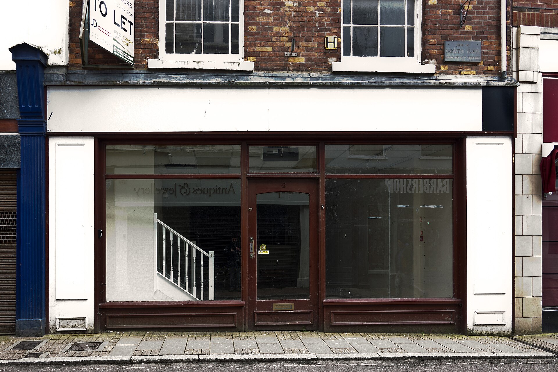 A quiet UK high street with vacant retail units and a small number of pedestrians